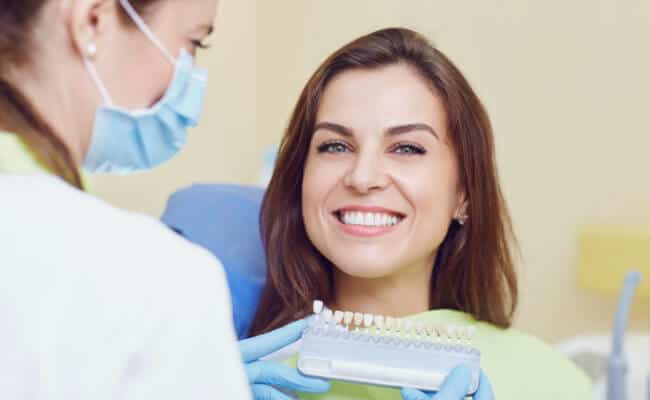 Implantes dentales en la sonrisa de paciente femenina, puestos por periodoncista mujer en consultorio.