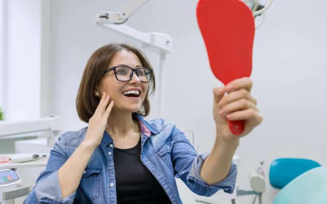 Mujer en un consultorio dental viendo su sonrisa en un espejo